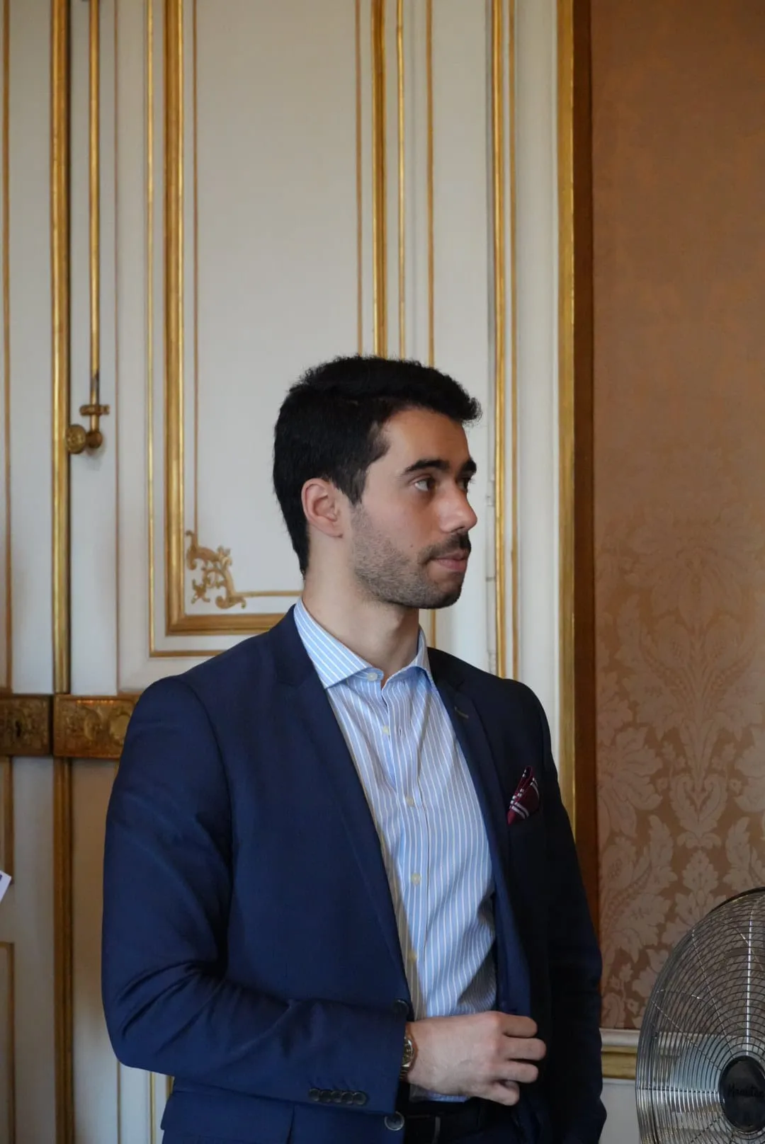 Portrait de Kevan Gafaïti, en costume, dans un salon aux boiseries dorées